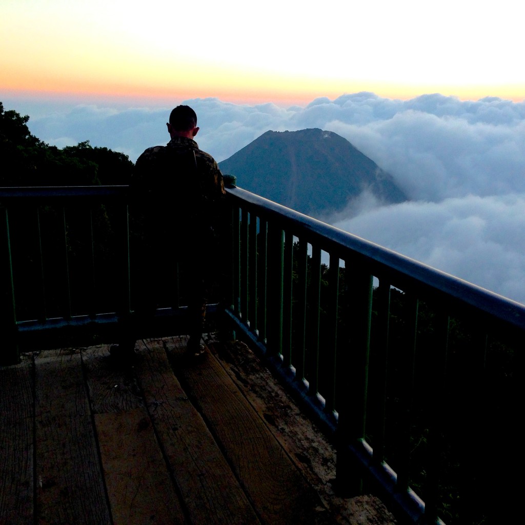 An armed guard checks his text messages while overlooking Volcan de Izalco